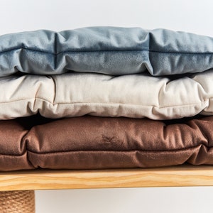 May include: Three cushions stacked on top of each other. The top cushion is light blue, the middle cushion is cream, and the bottom cushion is brown. The cushions are all made of a soft, plush fabric.
