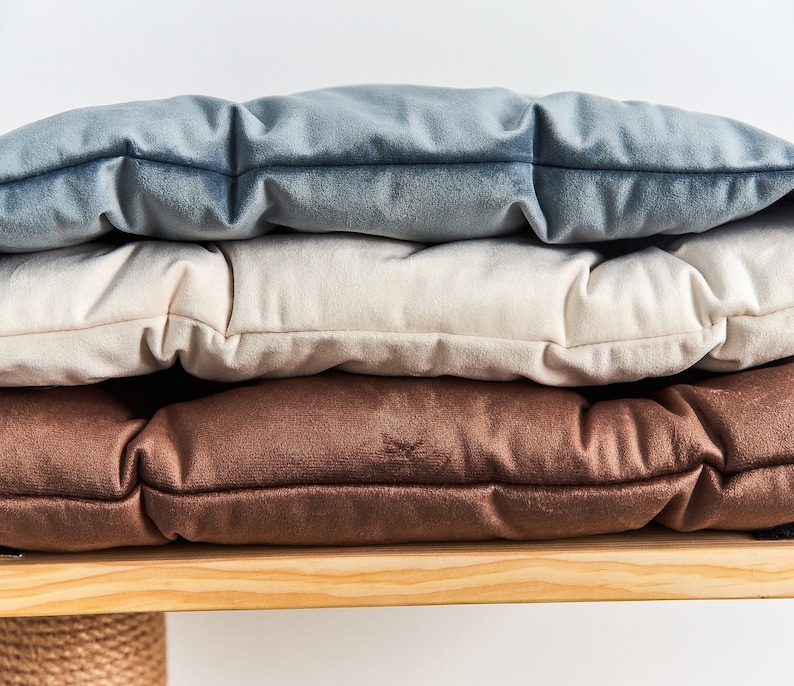 May include: Three cushions stacked on top of each other. The top cushion is light blue, the middle cushion is cream, and the bottom cushion is brown. The cushions are all made of a soft, plush fabric.