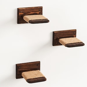 May include: Three brown wooden cat shelves with sisal rope surfaces mounted on a white wall.