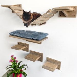 May include: A wooden cat tree with a bridge, a platform with a blue cushion, and three smaller platforms with sisal rope. A black cat is sitting on the bridge.