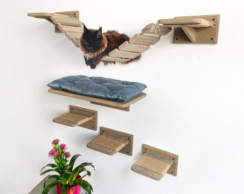 May include: A wooden cat tree with a bridge, a platform with a blue cushion, and three smaller platforms with sisal rope. A black cat is sitting on the bridge.