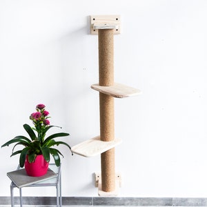 May include: A wall-mounted cat tree with three platforms and a sisal-covered scratching post. The platforms are made of natural wood and are unpainted. The cat tree is mounted to a white wall.