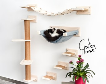 May include: A wall-mounted cat tree with a hammock, a scratching post, and multiple platforms. The cat tree is made of wood and has a natural finish. A black and white cat is sleeping in the hammock. The text "Gratsy Home" is written on the wall.
