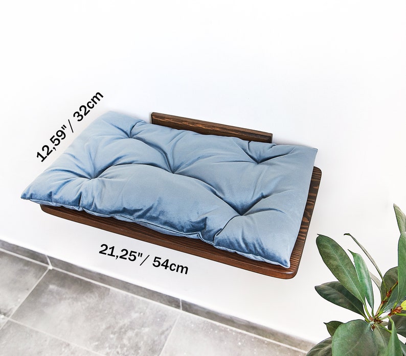 May include: A light blue, tufted cat bed mounted on a dark wood shelf. The shelf is 21.25 inches wide and 12.59 inches deep.