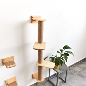 May include: A wooden cat tree with three platforms and a scratching post. The cat tree is mounted to a white wall. The platforms are made of natural wood and the scratching post is covered in sisal rope.