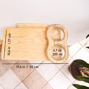 May include: A wooden cat feeder with two glass bowls. The feeder is 19.6 inches wide and 10.6 inches tall. The bowls are 6.7 ounces each and hold 200 ml of food or water.
