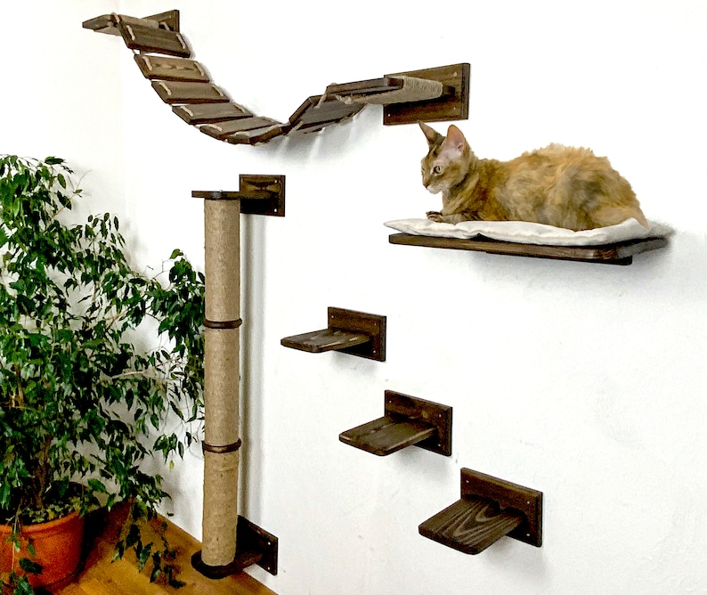 Pu&ograve; includere: Un albero per gatti a parete con un palo per grattare rivestito in sisal, un ponte e pi&ugrave; ripiani. Un gatto &egrave; seduto su uno dei ripiani.