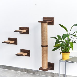 May include: A wall-mounted cat scratching post with a sisal-covered scratching post and three platforms. The scratching post is made of dark brown wood and the platforms are covered in brown sisal rope. A potted plant is in the background.