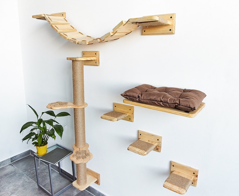 May include: A wooden cat tree with a scratching post, a bridge, and a bed. The cat tree is mounted on a white wall. The bridge is curved and has a natural wood finish. The bed is rectangular and has a brown cushion. The cat tree is made of natural wood and has a rustic look.