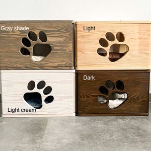 May include: Four wooden cat beds in different shades of brown, gray, and cream. Each bed has a paw-shaped opening and a soft cushion inside. The beds are labeled "Gray shade", "Light", "Light cream", and "Dark".