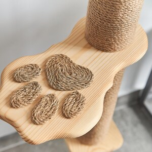 May include: A wooden cat scratching post with a paw-shaped platform. The platform has four rope paw prints and a larger heart-shaped rope print.