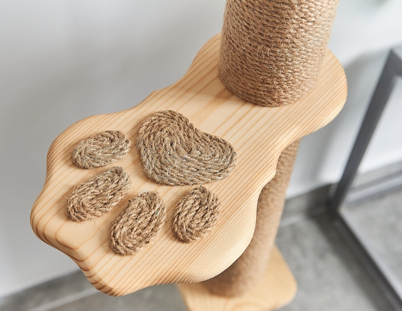 May include: A wooden cat scratching post with a paw-shaped platform. The platform has four rope paw prints and a larger heart-shaped rope print.