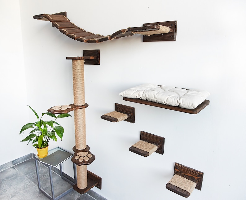 May include: A wall-mounted cat tree with a sisal-covered scratching post, a bridge, a bed, and several platforms. The platforms are covered in sisal rope and have paw print cutouts. The bed has a white cushion.