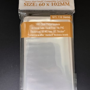 May include: A package of 110 clear card sleeves for trading cards. The sleeves are made of polypropylene and are archival safe, acid free, and PVC free. The sleeves are 60 microns thick, which is 50% thicker than standard sleeves. The package is labeled "Sleeve Kings" and "Space Alert Small" Compatible Card Sleeves. The size of the sleeves is 60 x 102 mm.