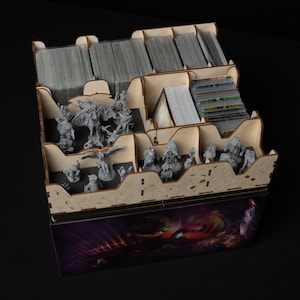 May include: A wooden game organizer with multiple compartments, filled with stacks of cards and miniature figurines. The organizer has a decorative front panel with a colorful illustration. The compartments are designed to hold various game components.