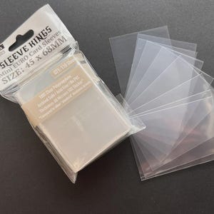May include: A package of clear plastic card sleeves with the text "SLEEVE KINGS" and "Mini EURO Card Sleeves" with dimensions of 45 x 68mm. A stack of individual sleeves is fanned out beside the package. The package contains 110 sleeves.