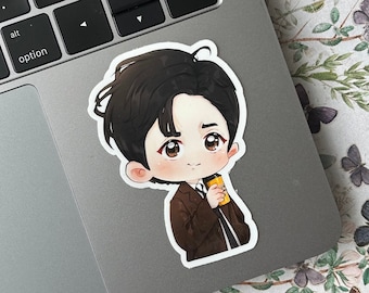May include: A sticker of a cartoon man with brown hair, wearing a brown jacket and holding a yellow cup. The sticker is on a silver laptop.