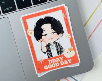 May include: A red and white sticker with a cartoon illustration of a person with black hair and a cat. The text "DDAY GOOD DAY" is printed on the sticker.
