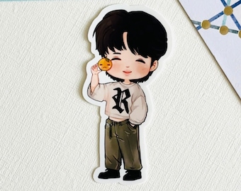May include: A cartoon illustration of a person with black hair wearing a white shirt with a black letter R on it, green pants, and black shoes. The person is holding a small yellow circle with a sad face in their right hand.