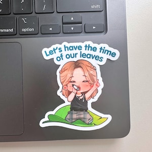 May include: A die-cut sticker featuring a cartoon character with light brown hair, wearing a black tank top and plaid pants, holding a microphone. The character sits on a large green leaf. The text above reads, Let's have the time of our leaves.