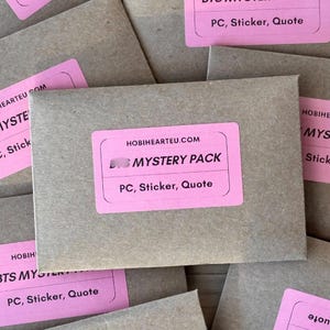 May include: Several brown paper envelopes with pink labels. The labels read "HOBIEARTEU.COM MYSTERY PACK PC, Sticker, Quote". The envelopes are stacked together, with some labels partially visible.
