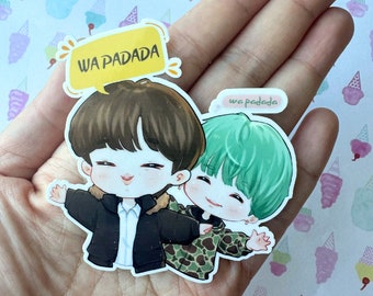 Pode incluir: Um adesivo com dois personagens de desenho animado, um com cabelo castanho e uma jaqueta preta, e o outro com cabelo verde e uma jaqueta camuflada. O adesivo tem o texto "WA PADADA" em um balão de fala amarelo.
