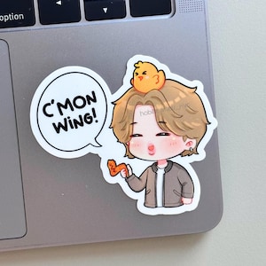 May include: A sticker depicting a cartoon character with light brown hair, wearing a grey jacket, and holding a chicken wing. A yellow chick sits on the character's head. The speech bubble says, "C'MON WING!"