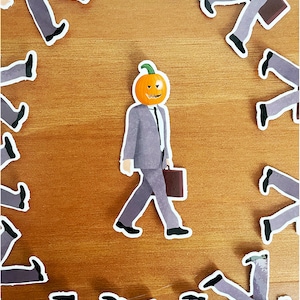 Puede incluir: Un grupo de figuras grises con traje y cabezas de calabaza caminando en círculo sobre un fondo de madera.