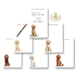 May include: A collection of white rectangular notepads featuring watercolor illustrations of various doodle dogs. Each notepad displays a unique name or family title in colored text. A black pen rests on one notepad. The logo Lula Merle is visible.