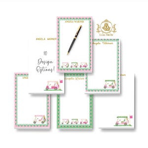 May include: A collection of rectangular paper notepads featuring a pink golf cart illustration, a green and pink patterned border, and the name Angela Warner printed in gold. One notepad includes the text 10 Design Options! and a black pen.