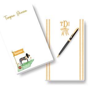May include: Two white rectangular notepads. The left notepad features the name Teagan Dineen in gold script and a graphic of a hound dog, a football, and a flag labeled Tennessee. The right notepad has a gold monogram TDI with a bow and a black pen.