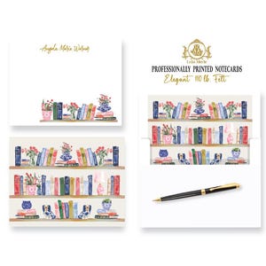 May include: White stationery notecards featuring a watercolor illustration of bookshelves filled with colorful books, vases of flowers, and small figurines. The text reads Angela Maria Warner, Isla Merle, PROFESSIONALLY PRINTED NOTECARDS, and Elegant 110 lb. Felt.