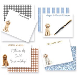 May include: A collection of rectangular white notecards featuring watercolor illustrations of golden-colored dogs. The cards display various names and text including Linda Adams, Angela & Patrick Warner, Angela Warner, The Adams Family, and Notecards Sold Separately. A black pen rests on one card, and several cards are paired with patterned envelopes in black gingham, blue stripes, brown gingham, and blue floral prints.