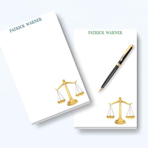 May include: Two white rectangular notepads featuring the name PATRICK WARNER printed at the top. One notepad has the name in blue, the other in green. Both feature a gold-colored illustration of a scale of justice and a black ballpoint pen.