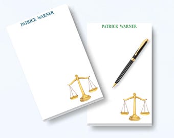 May include: Two white rectangular notepads featuring the name PATRICK WARNER printed at the top. One notepad displays the name in blue, the other in green. Both feature a gold-colored illustration of a scale of justice and a black ballpoint pen.