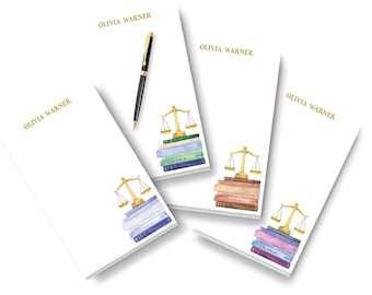 May include: Four white rectangular notepads with the name OLIVIA WARNER printed in gold at the top. Each notepad features a watercolor illustration of a gold scale of justice resting on a stack of colorful books. A black and gold pen is included.