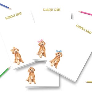 May include: Three white rectangular notepads with the name KIMBERLY KIRBY printed in gold at the top. Each notepad features a watercolor illustration of a brown curly-haired dog wearing a small checkered bow on its head in various colors.