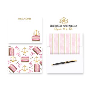 May include: A set of professionally printed notecards with a pink and gold striped envelope. The notecards feature a watercolor design of books, scales of justice, and pink ribbons. The text on the envelope reads "Professionally Printed Notecards Elegant 110 lb Felt".