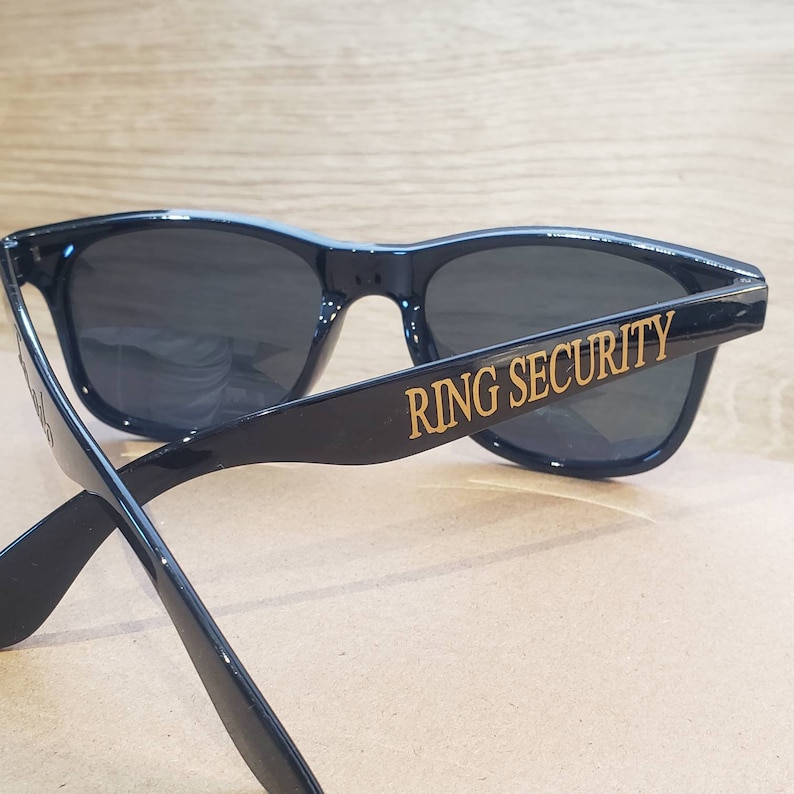 May include: Black sunglasses with the words "RING SECURITY" printed in gold on the right arm.
