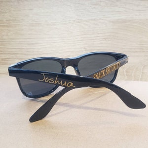 May include: Black sunglasses with the text "Snack Security" on one arm and the name "Joshua" on the other arm.