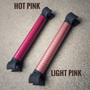 May include: Two carbon fiber rods with black end caps. The rod on the left is hot pink and the rod on the right is light pink.  "HOT PINK" and "LIGHT PINK" are written in brown text above the rods.
