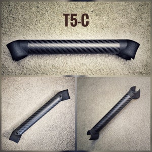 May include: A black carbon fiber grab handle with a T5-C label. The handle has a curved shape and is designed for use in a vehicle.