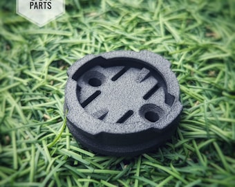 May include: Black plastic Quadlock Garmin Combo Insert. The insert is circular with a textured surface and a small hole in the centre.