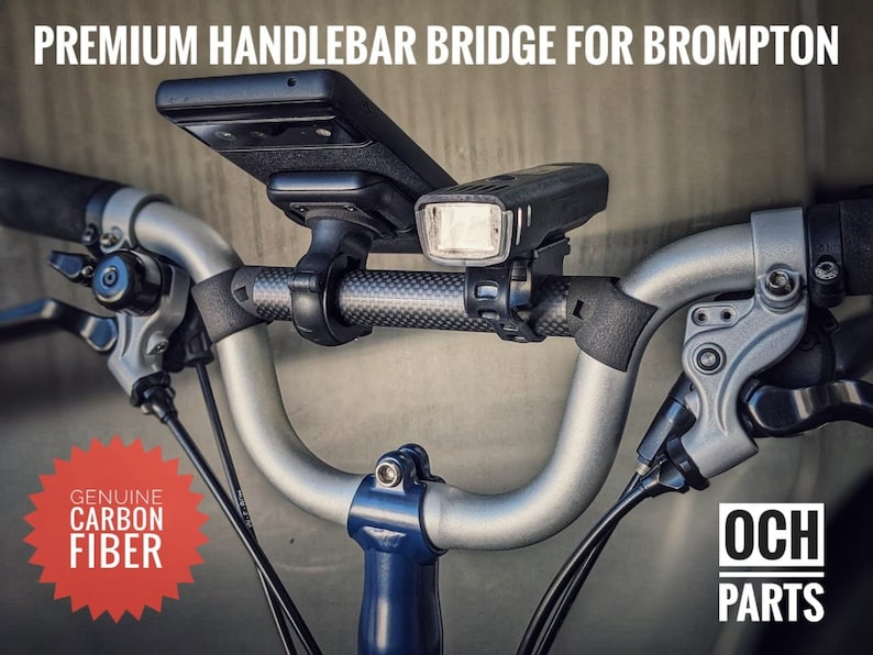 May include: A silver handlebar bridge for a Brompton bicycle with a black carbon fiber handlebar, a black phone mount, and a black bike light. The text "Genuine Carbon Fiber" is on a red starburst sticker. The text "OCH Parts" is on a white rectangle with a black border.