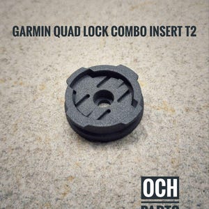 May include: A dark gray Garmin Quad Lock Combo Insert T2. The circular insert has a textured surface with a central hole and angled slots. The text "GARMIN QUAD LOCK COMBO INSERT T2" is above the insert. The logo "OCH PARTS" is below.