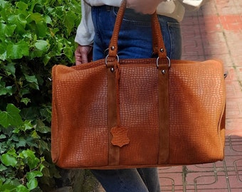 Könnte beinhalten: Eine braune Ledertasche mit strukturierter Oberfläche. Die Tasche hat zwei Tragegriffe oben und einen abnehmbaren Schultergurt.