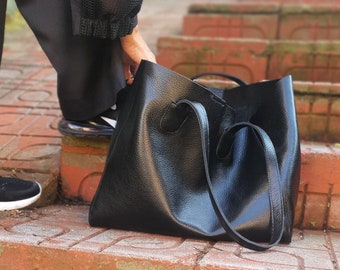 May include: A black leather tote bag with two handles. The bag is sitting on a set of brick steps.