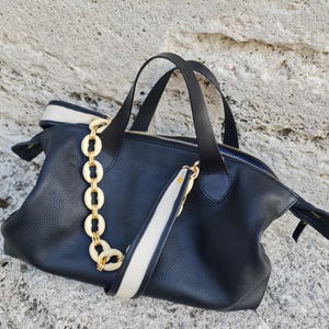 May include: A black leather tote bag with a white and black strap and a gold chain detail.