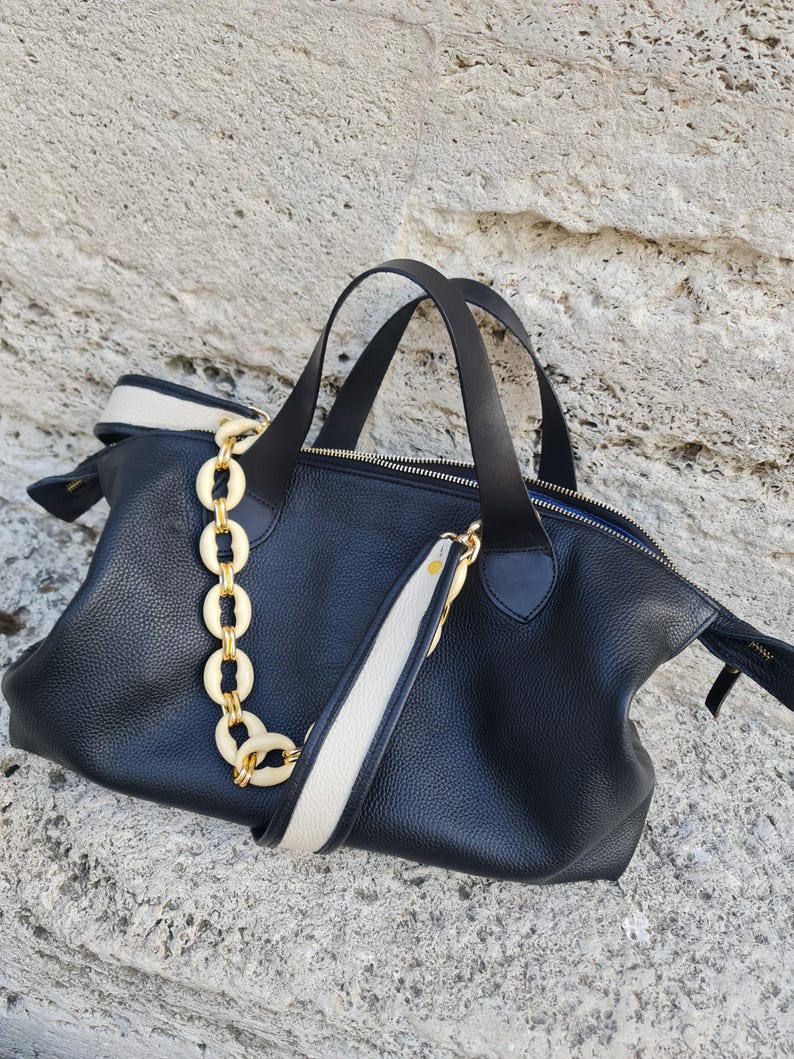 May include: A black leather tote bag with a white and black strap and a gold chain detail.