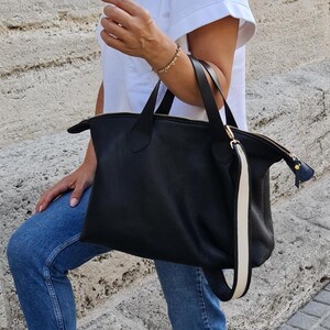 May include: A black leather tote bag with a white stripe on the strap. The bag has a zipper closure and gold hardware.